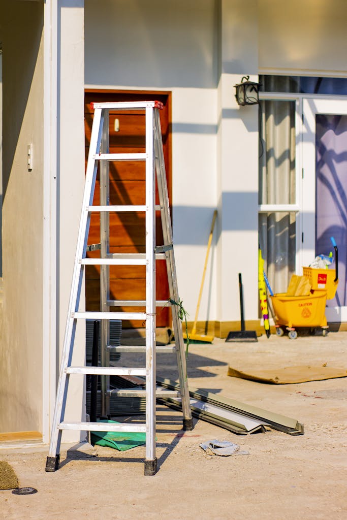 An outdoor home renovation scene featuring a ladder and various tools indicating ongoing construction work.